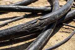 Close-up photo of aged outdoor power cable showing cracked sheath from ultraviolet radiation, thermal ageing and chemical erosion, intact black PE XLPE outdoor cable beside damaged cable for comparison, industrial cable product news cover, no text
